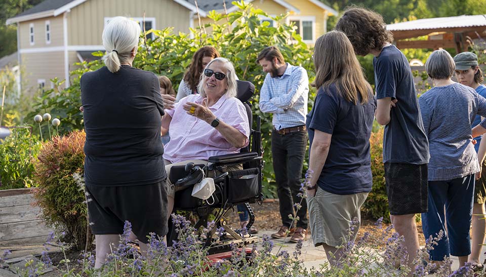 A woman in a wheelchair surrounded by neighbors in a garden.